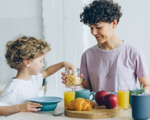 A mother and her son sharing a healthy breakfast at home, featuring cereal, juice, and milk.